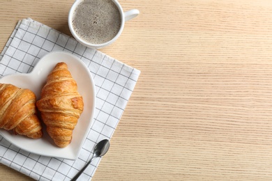 Plate of fresh croissants served on wooden table, flat lay with space for text. French pastry