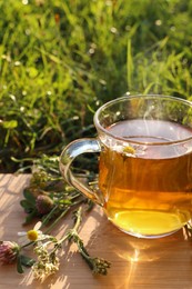 Cup of aromatic herbal tea and different wildflowers on wooden board in meadow