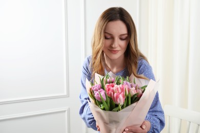 Young woman with bouquet of beautiful tulips indoors. Space for text