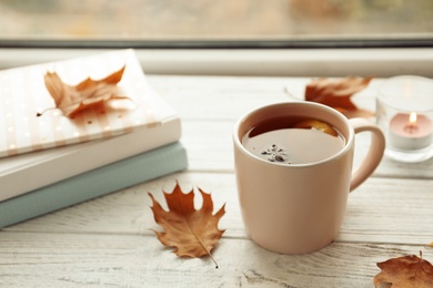 Photo of Cup of tea, autumn leaves and stack of books on windowsill