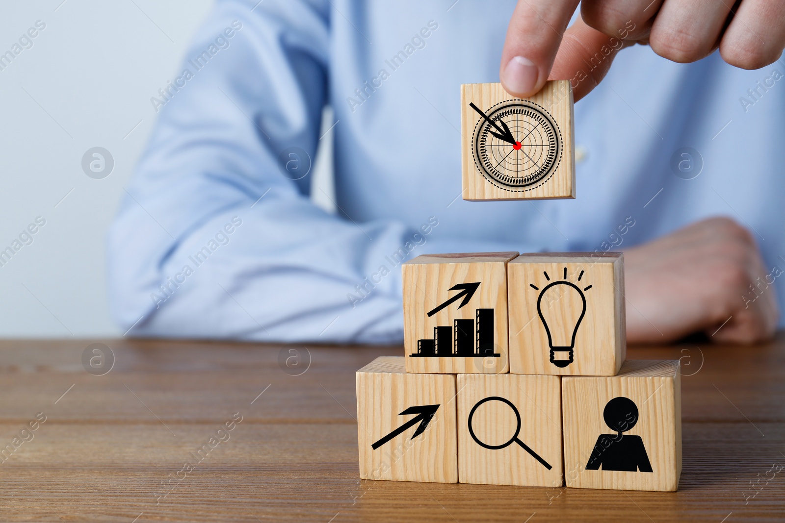 Image of Man building pyramid of cubes with icons on wooden table, closeup. Target, arrow, magnifier and other illustrations