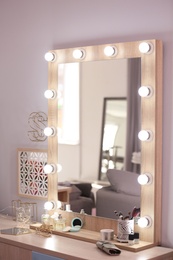 Photo of Mirror with light bulbs and cosmetic products on dressing table indoors
