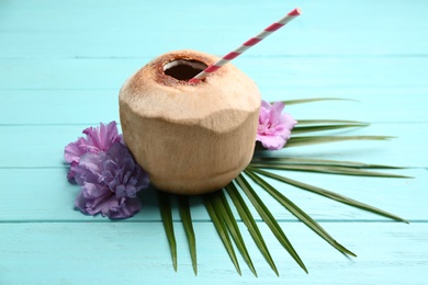 Photo of Young peeled coconut with straw, palm leaf and flowers on light blue wooden table