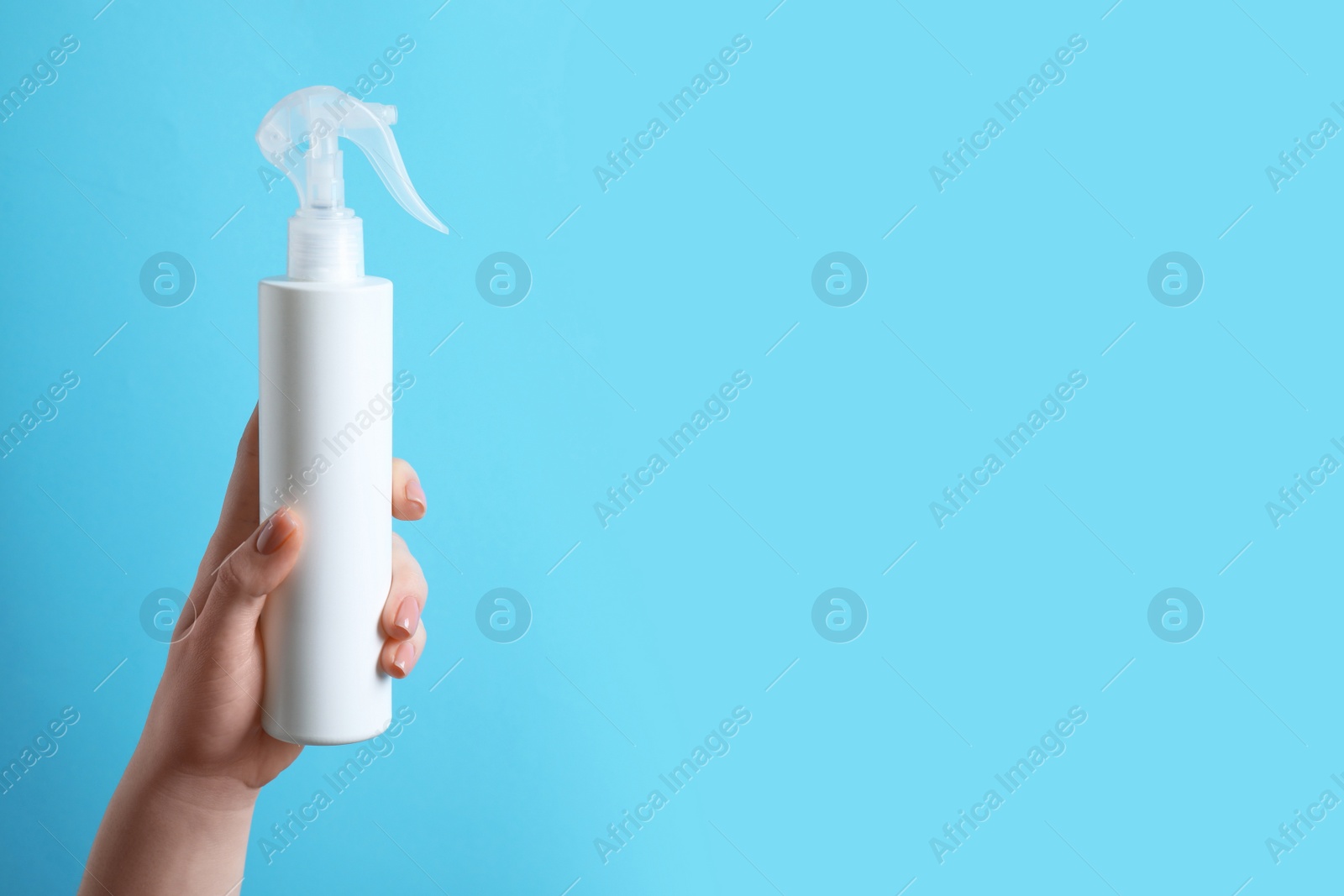 Photo of Woman holding spray bottle with thermal protection on light blue background, closeup. Space for text