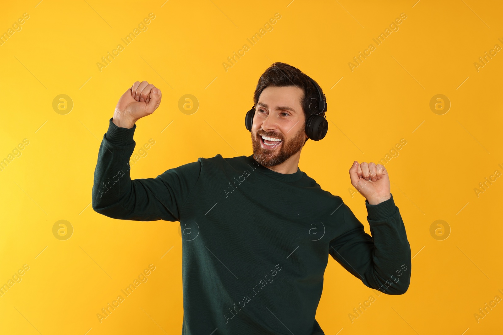 Photo of Happy man listening music with headphones on yellow background