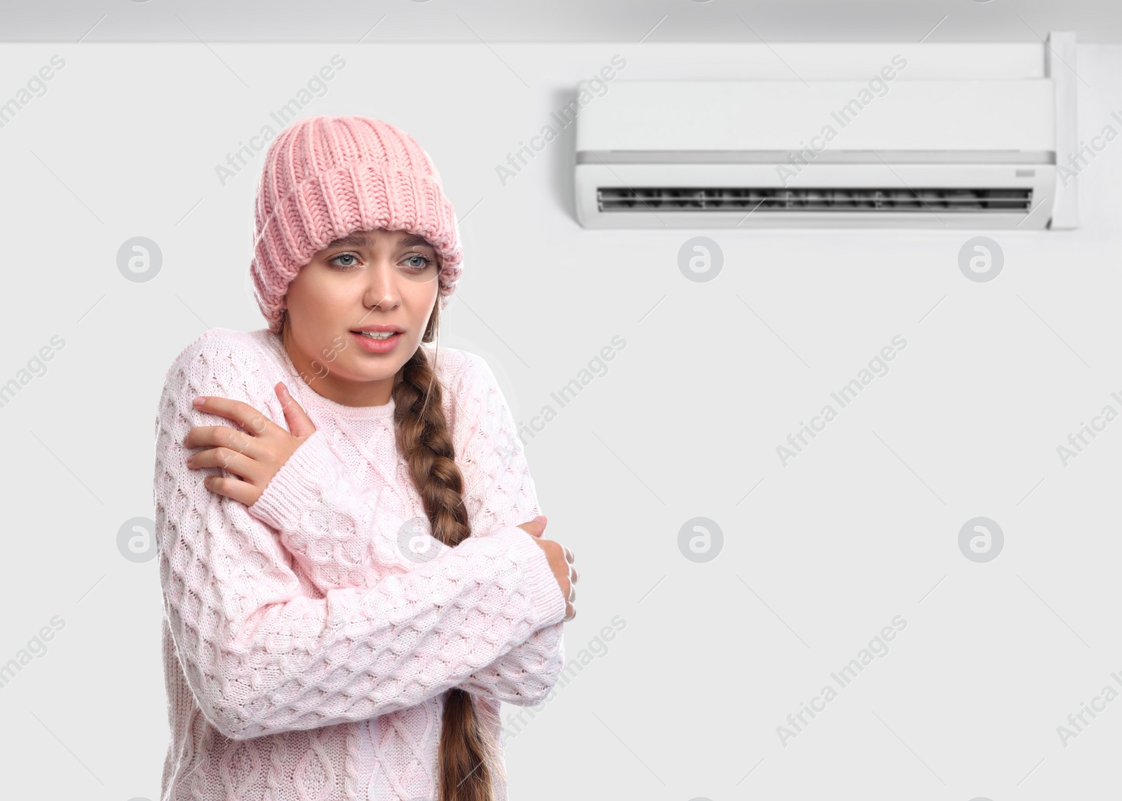 Image of Woman suffering from cold in room with air conditioner on white wall, space for text