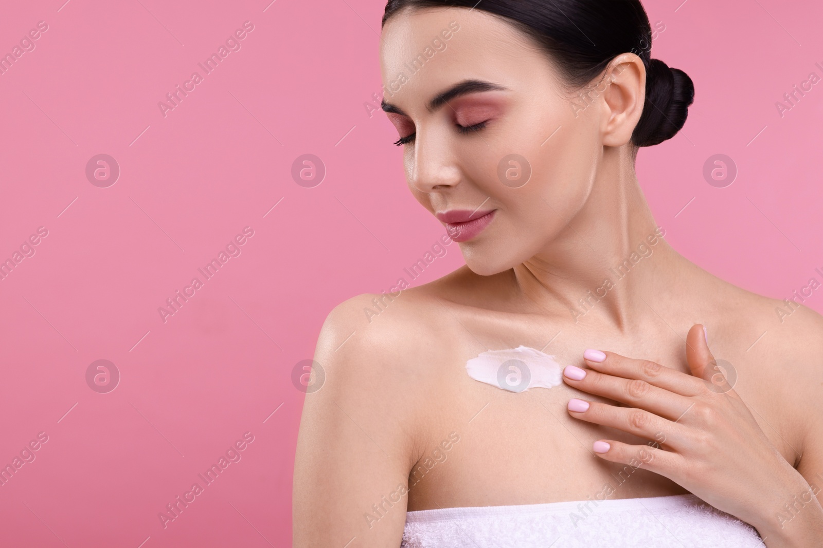 Photo of Beautiful woman with smear of body cream on her chest against pink background, space for text