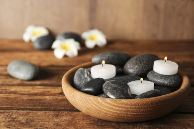 Wooden bowl with burning candles and spa stones on table