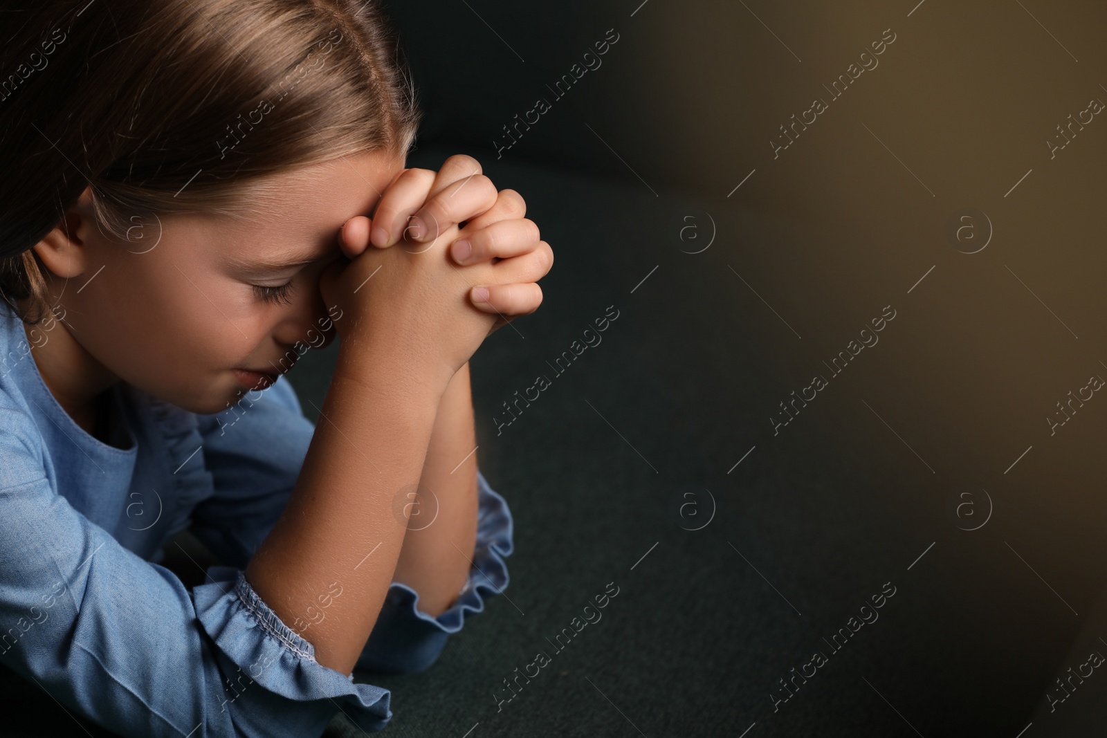 Photo of Cute little girl praying on dark green background, closeup. Space for text
