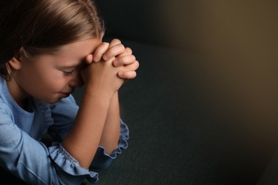 Photo of Cute little girl praying on dark green background, closeup. Space for text