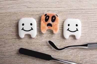 Photo of Clean and dirty plastic teeth with faces, dental tools on wooden table, flat lay