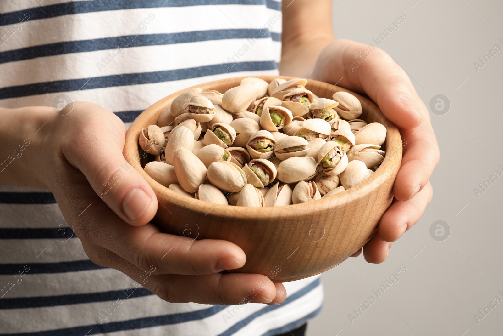 Photo of Woman holding bowl with pistachio nuts on light background, closeup