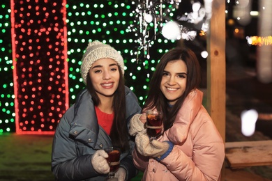 Friends with glass cups of mulled wine at winter fair