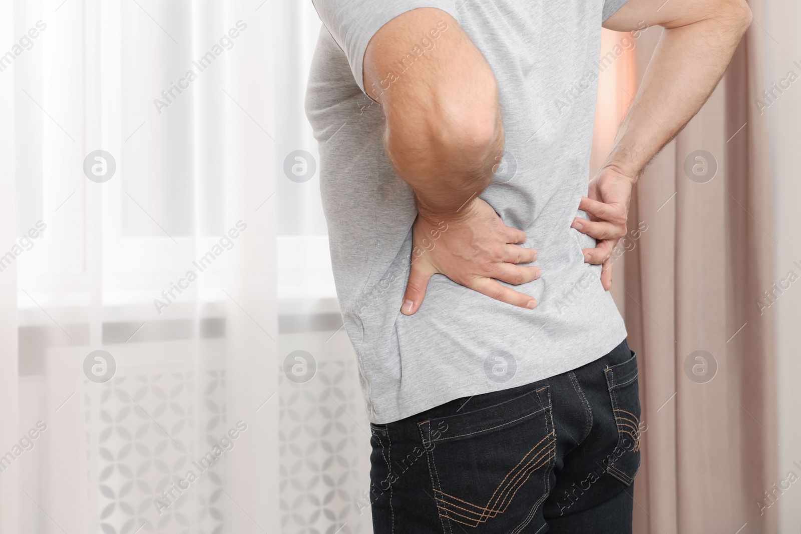 Photo of Man suffering from back pain indoors, closeup