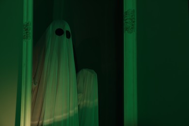 Photo of Creepy ghost. Woman covered with sheet in green light, reflection in mirror