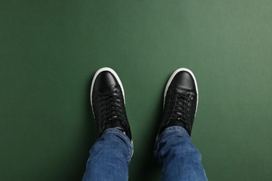Man in stylish sneakers standing on green background, top view