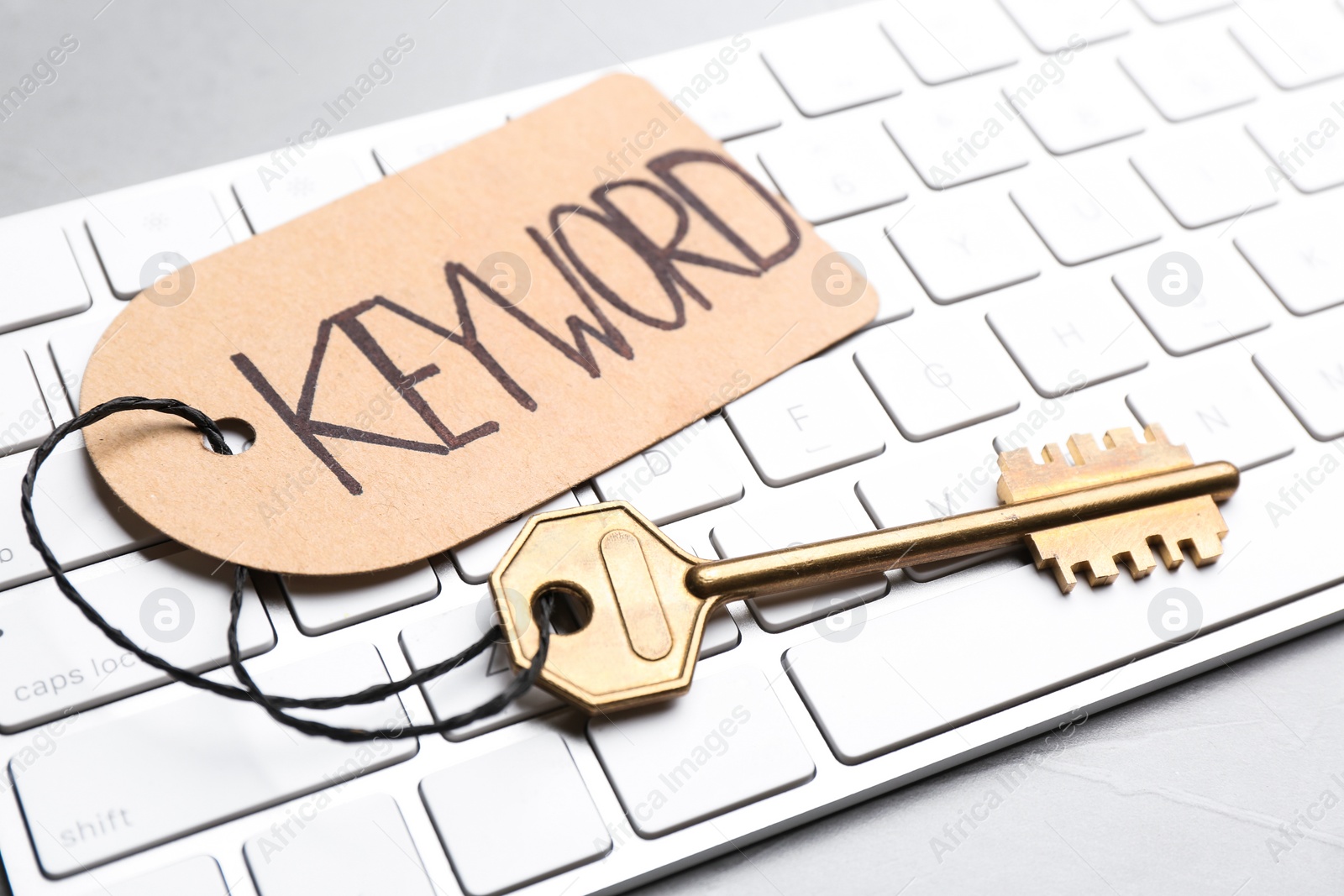 Photo of Key with tag KEYWORD and computer keyboard on table, closeup