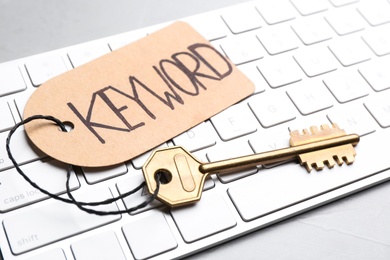 Key with tag KEYWORD and computer keyboard on table, closeup