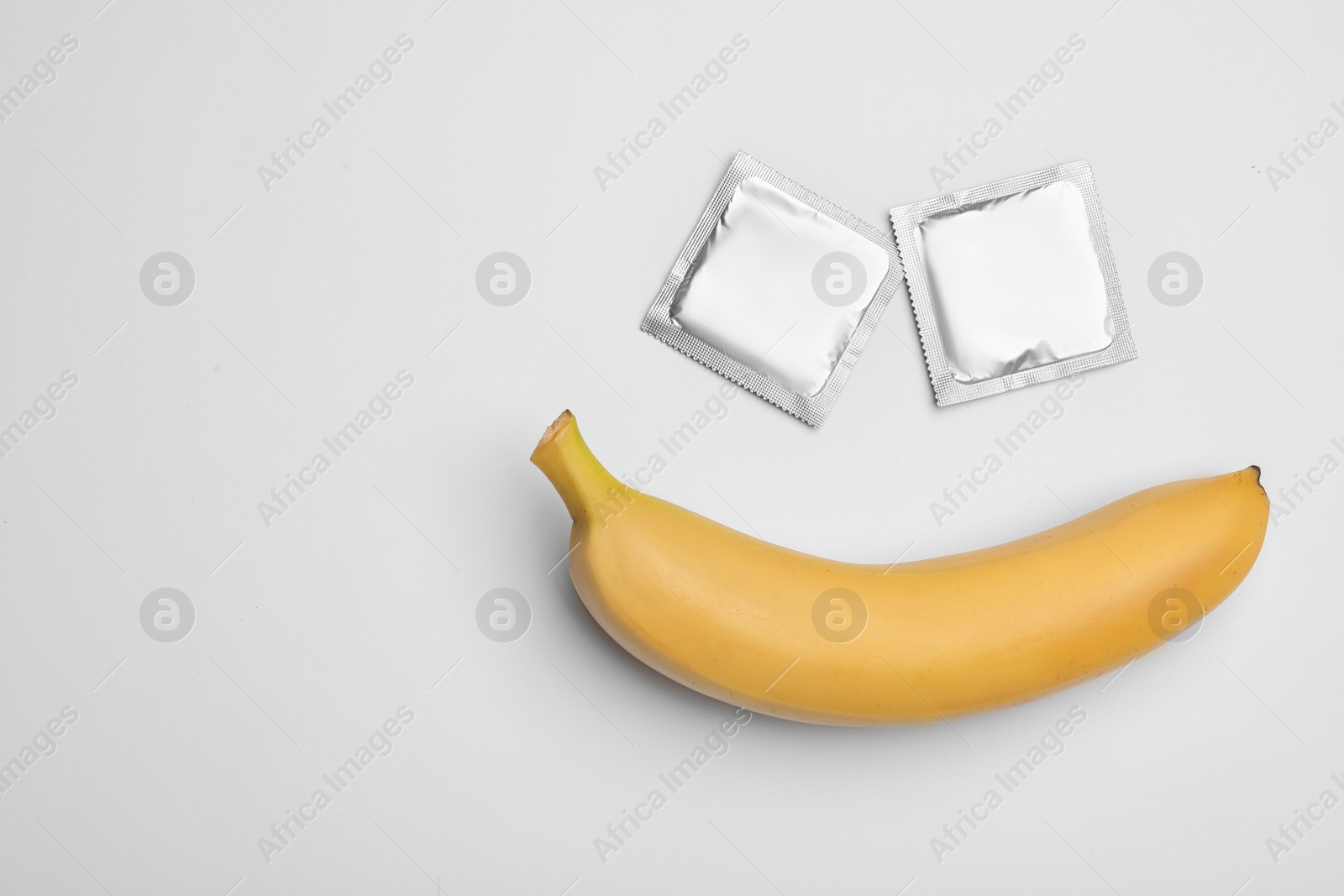 Photo of Condoms and banana on white background, top view. Safe sex