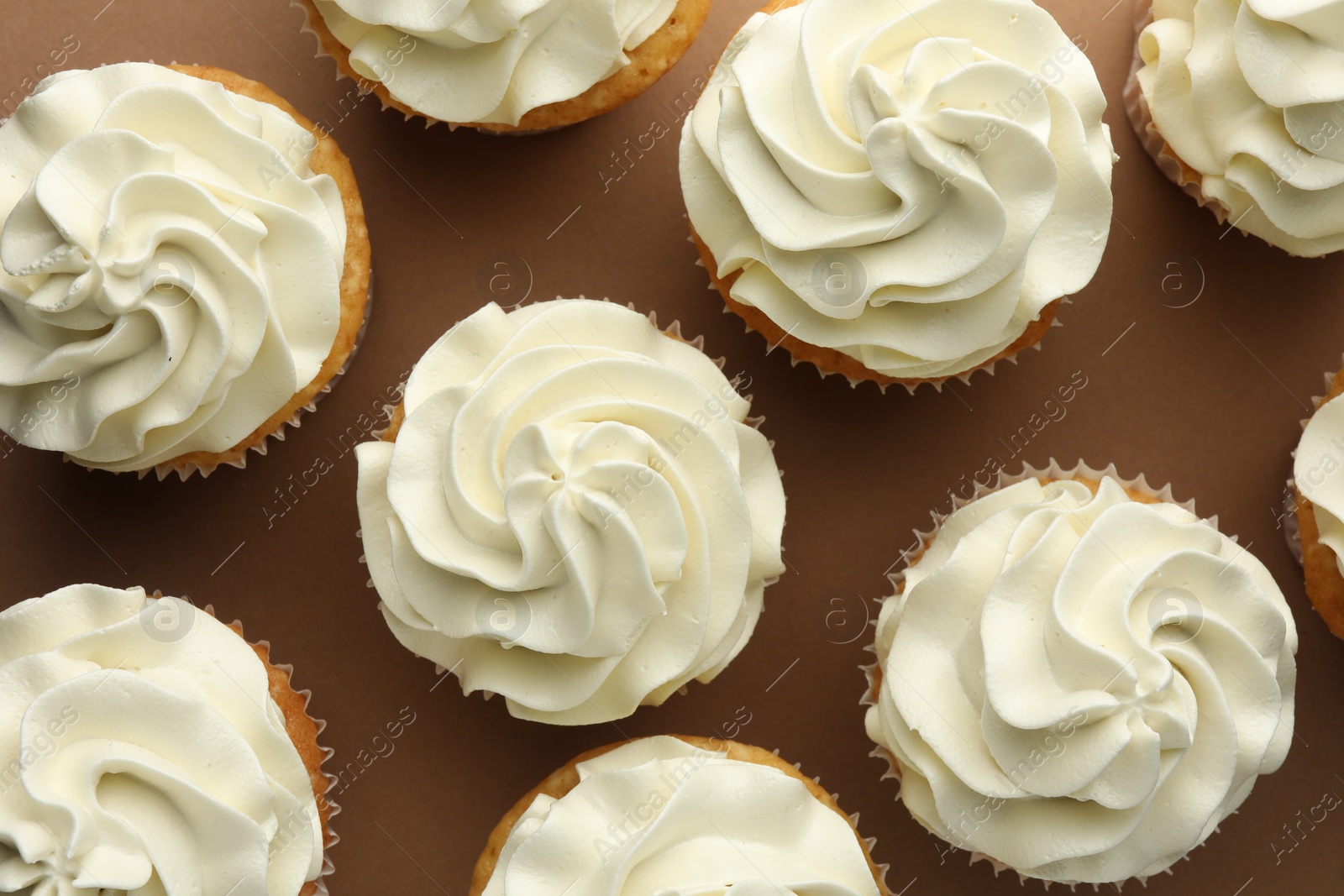 Photo of Tasty vanilla cupcakes with cream on dark beige background, top view