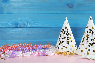 Photo of Colorful serpentine streamers, party hats and confetti on pink wooden table. Space for text