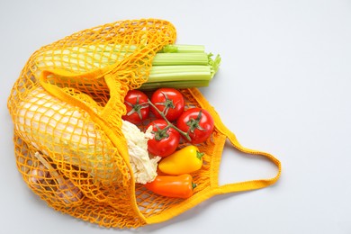 Photo of String bag with different vegetables on light grey background, top view