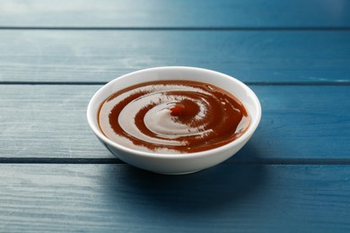 Photo of Tasty barbeque sauce in bowl on blue wooden table