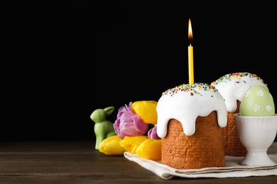 Photo of Traditional Easter cakes and one with burning candle on wooden table against black background. Space for text