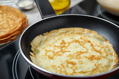 Photo of Delicious thin pancake in frying pan on induction stove, closeup