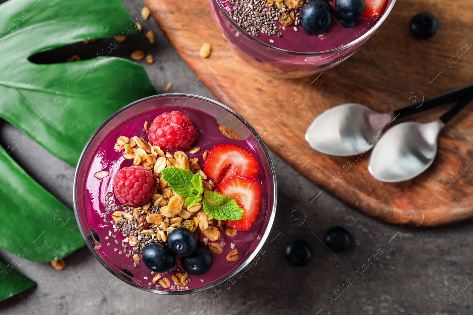 Photo of Delicious acai dessert with granola and berries served on grey table, flat lay. Space for text