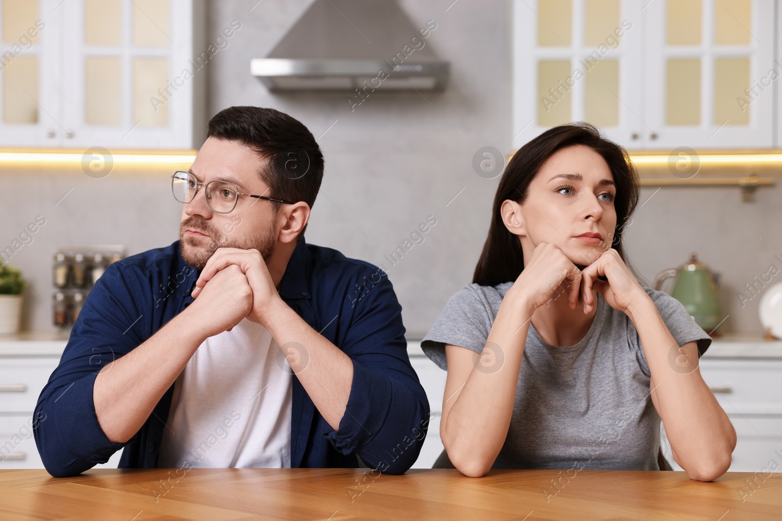 Photo of Offended couple ignoring each other after quarrel at table in kitchen. Relationship problems