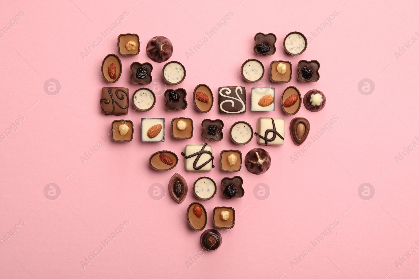 Photo of Heart made with delicious chocolate candies on pink background, top view