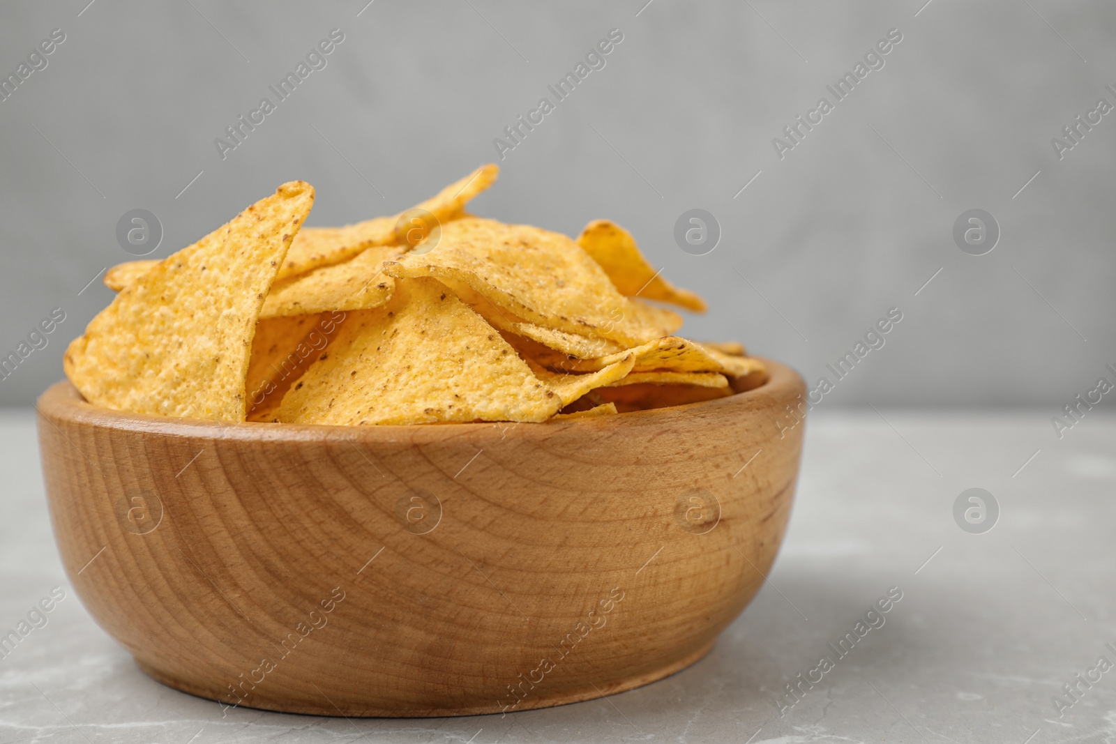 Photo of Wooden bowl with tasty Mexican nachos chips on grey table, closeup view. Space for text