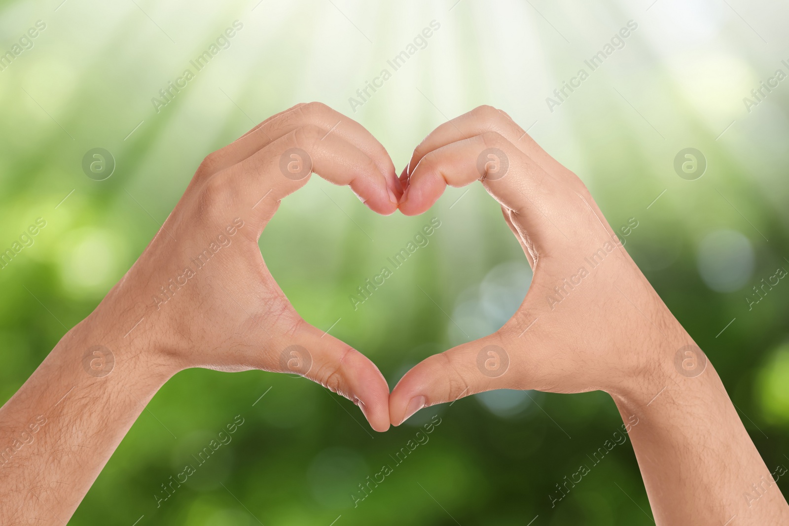 Image of Man making heart with hands outdoors on sunny day, closeup