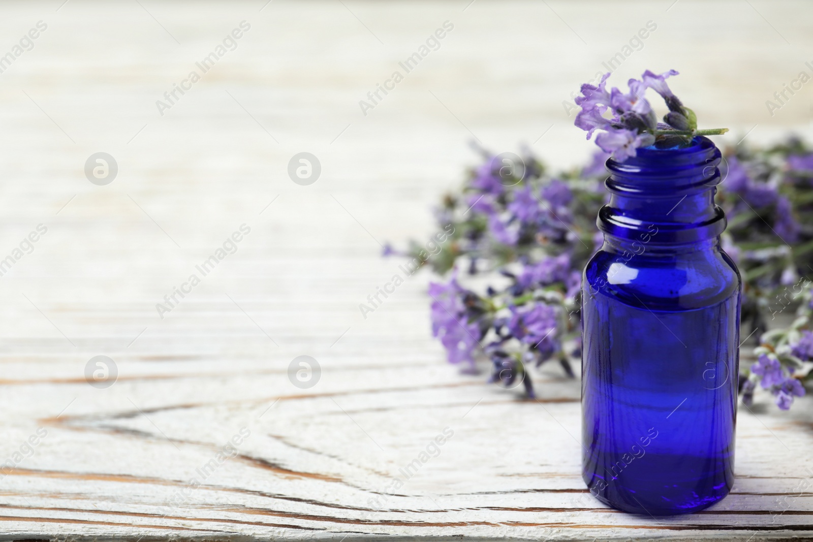 Photo of Bottle of essential oil and lavender flowers on white wooden table. Space for text