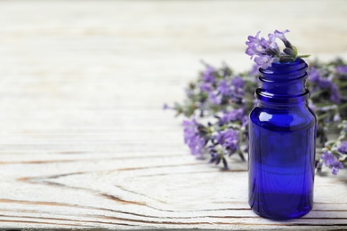 Photo of Bottle of essential oil and lavender flowers on white wooden table. Space for text