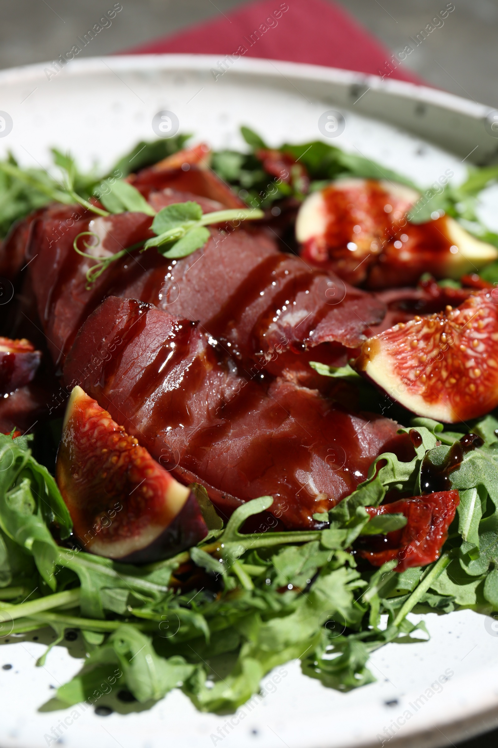 Photo of Tasty bresaola salad with figs, sun-dried tomatoes and balsamic vinegar on plate, closeup