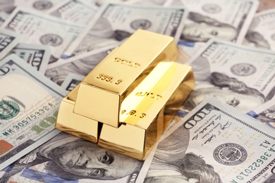 Photo of Shiny gold bars on pile of dollar bills