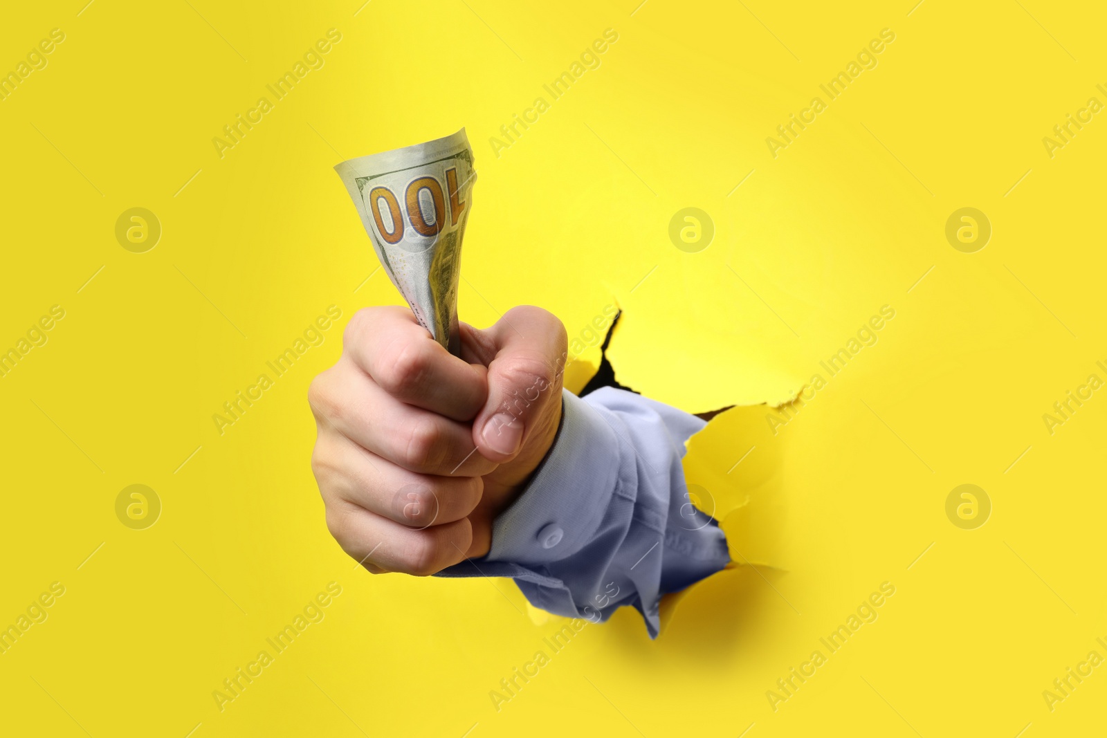 Photo of Businessman breaking through yellow paper with money in fist, closeup