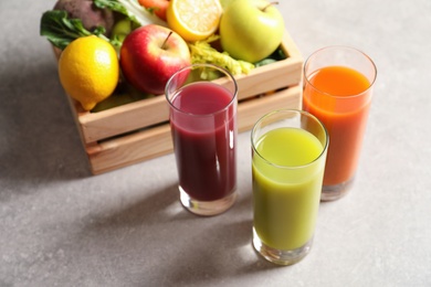 Glasses of different juices and wooden crate with fresh ingredients on table