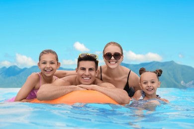 Image of Happy family in outdoor swimming pool at luxury resort with beautiful view of mountains on sunny day