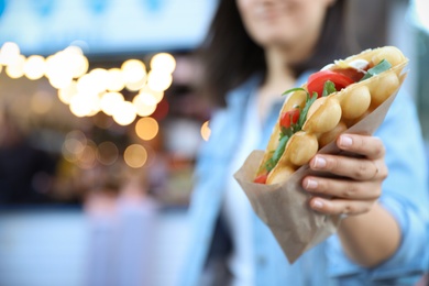 Photo of Young woman holding delicious bubble waffle with tomato and arugula outdoors, closeup