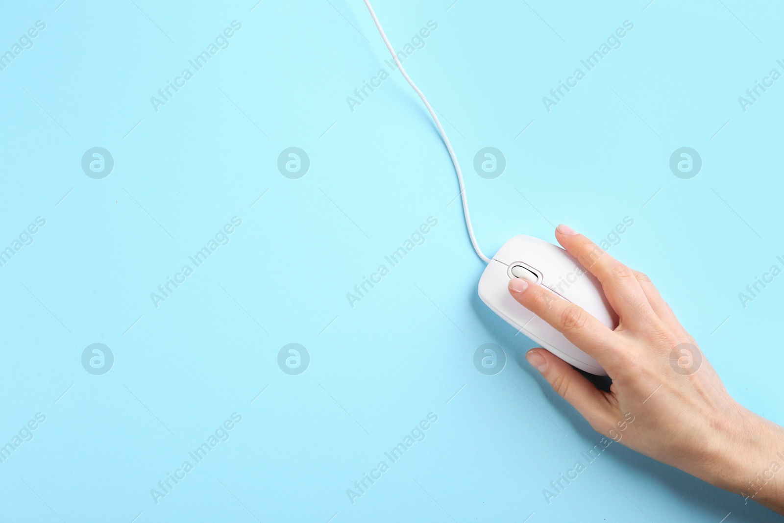 Photo of Woman using modern wired optical mouse on light blue background, top view. Space for text