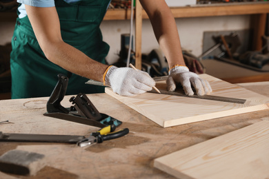 Photo of Professional carpenter measuring wooden board in workshop, closeup