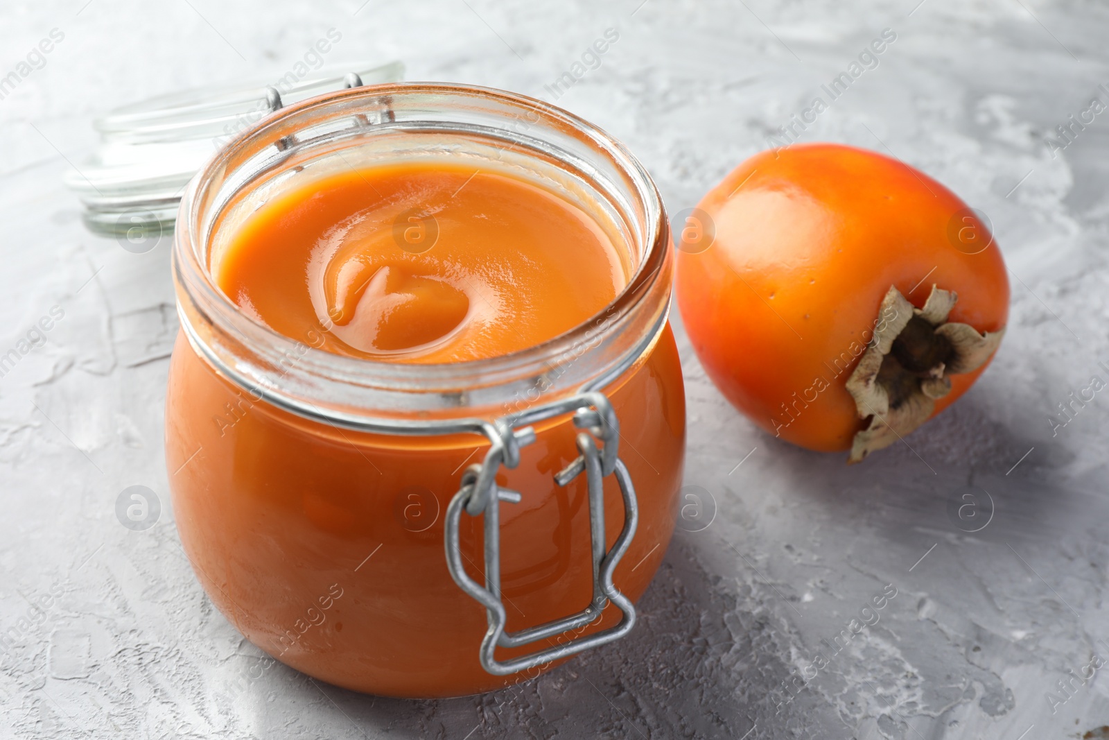 Photo of Delicious persimmon jam and fresh fruit on grey table, closeup