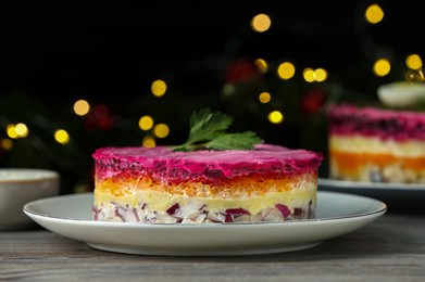 Photo of Herring under fur coat salad on white wooden table against blurred festive lights, space for text. Traditional Russian dish