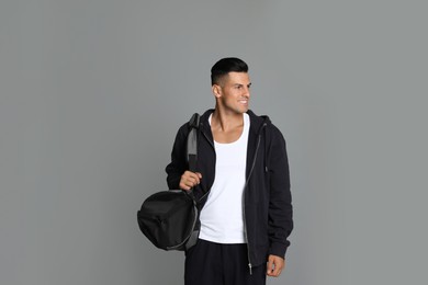 Handsome man with sports bag on grey background