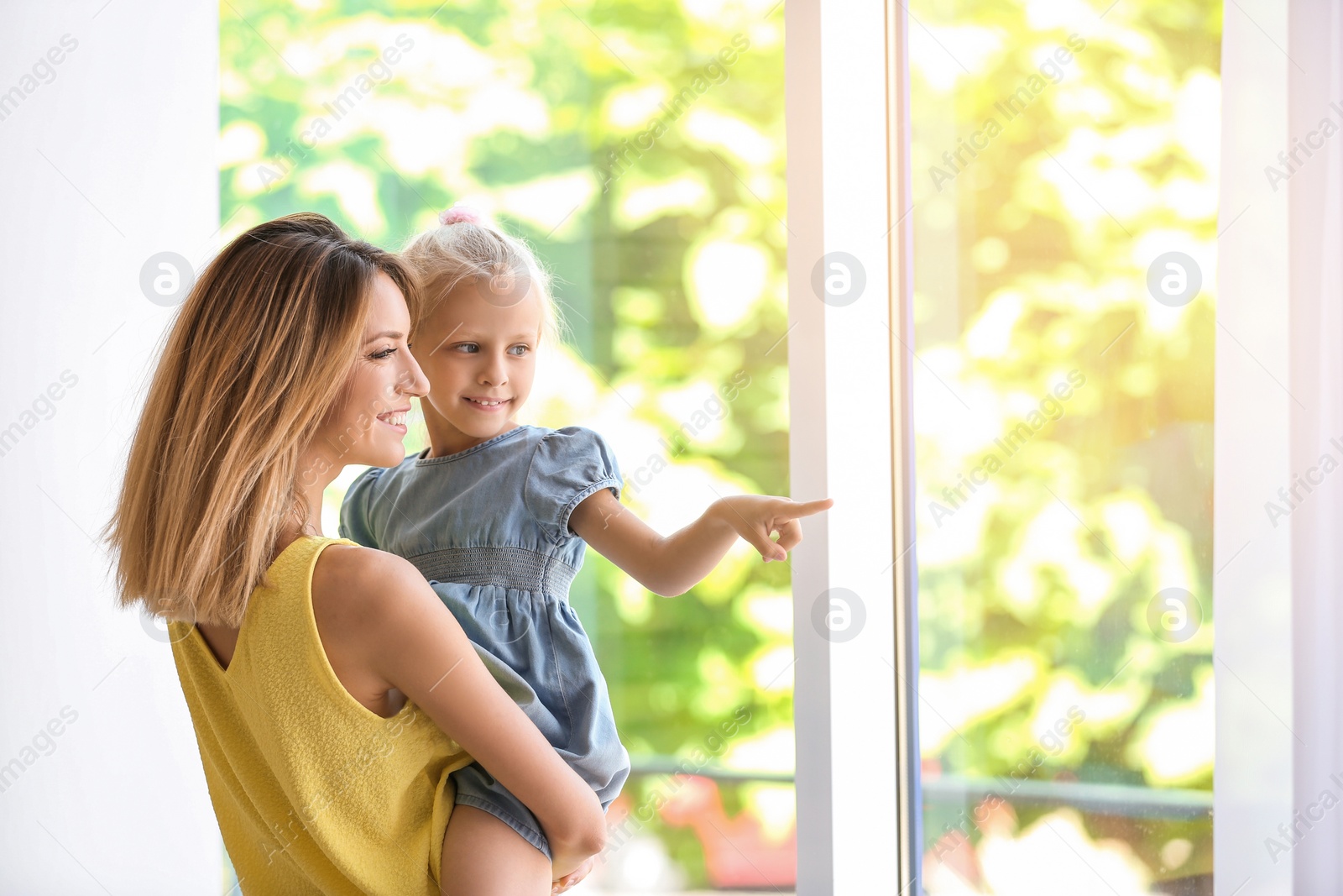 Photo of Young woman with cute little girl near window at home