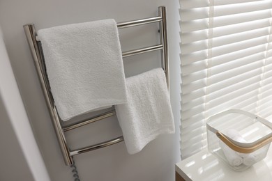 Photo of Heated rail with towels on white wall in bathroom