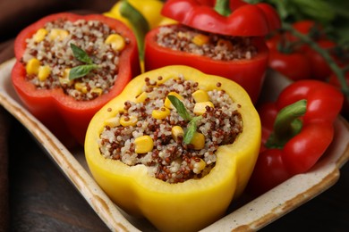 Photo of Quinoa stuffed bell peppers and basil in baking dish on wooden table, closeup